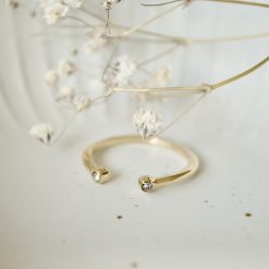 Goldfarbener Zirkonia-Ring in Schale mit weißen Trockenblumen