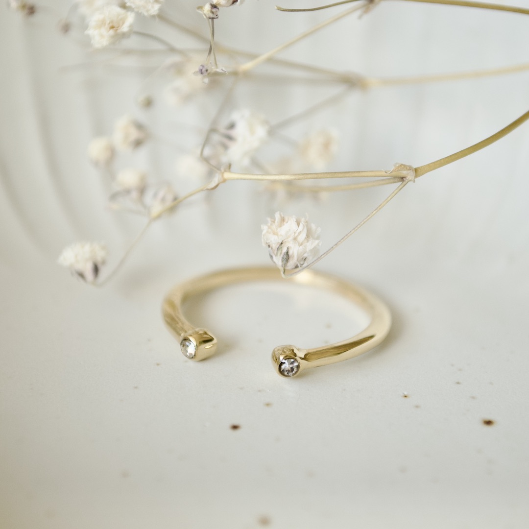 Goldfarbener Zirkonia-Ring in Schale mit weißen Trockenblumen