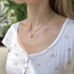 Kaurimuschel Kette Edelstahl in Gold – getragen von Frau mit weißem Leiber seitlich vor Pflanzen