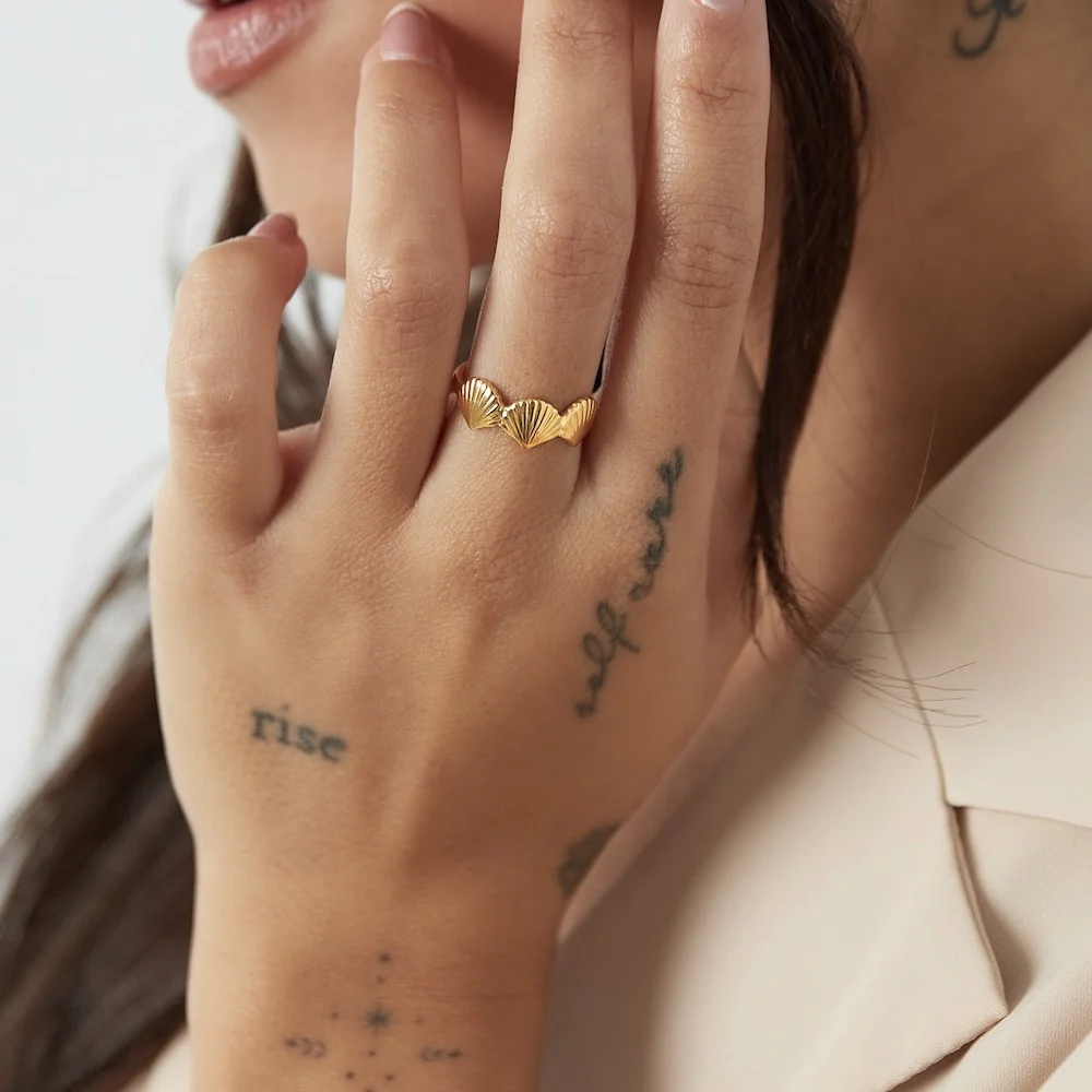 Goldener Muschel Ring aus Edelstahl an Frauenhand, am Mittelfinger getragen und vor das Gesicht gehalten