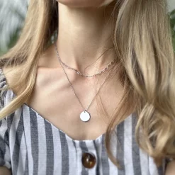 Detailaufnahme der silbernen Edelstahlkette mit rundem Gravuranhänger an einer Frau im Outdoor-Look